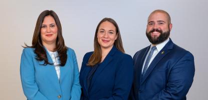 A woman in a light blue suit and women and man in dark blue suits pose side by side in