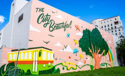blue sky in the background, a pink mural at Mcbride Plaza depicting a large tree with umbrellas and birds and a trolley